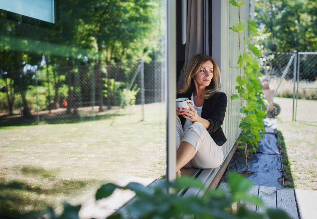 Front view of mature woman working in home office in container house in backyard, resting.