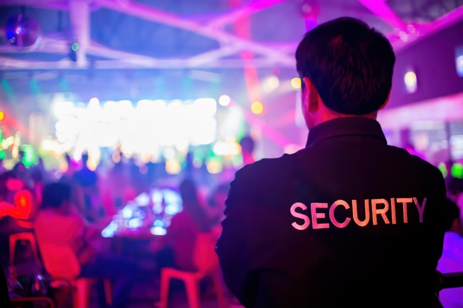 A man with his back to the camera in a brightly coloured room, with the word security written on the back of his jacket